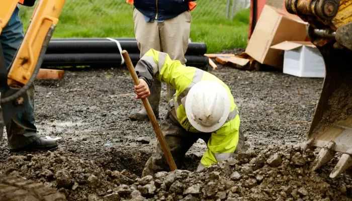 Worker using a small tracked excavator to dig a hole to fix a water leak at a large commercial housing development in Oregon to do a perc test