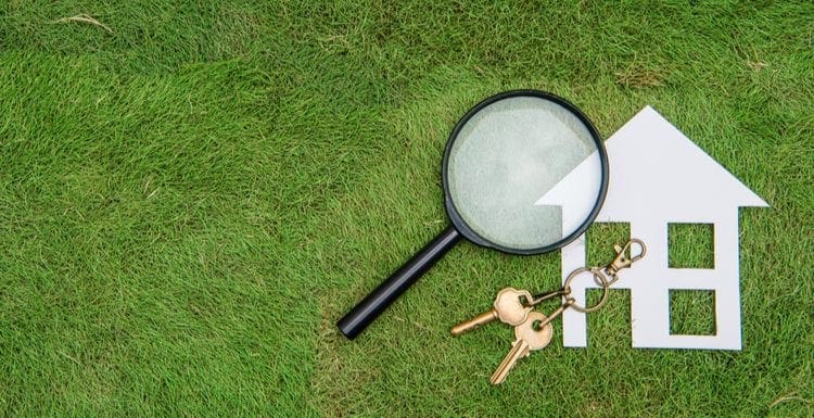 Paper 2d home and magnifying glass sit on a green grass lawn as a featured image for a piece on home inspector insurance