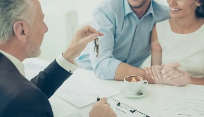 Close up of real estate agent giving keys to couple of customers
