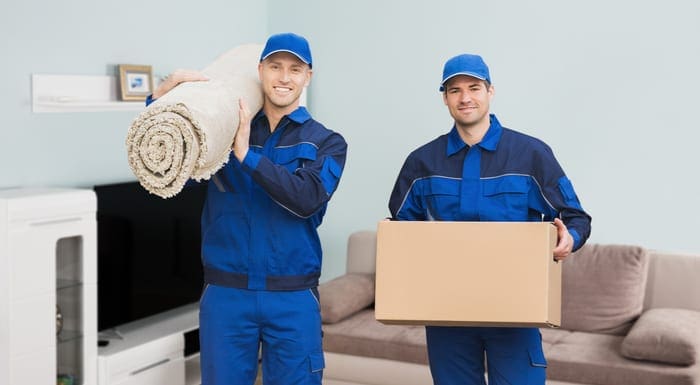 Portrait Of A Two Male Movers Carrying Rolled Carpet And Cardboard Box In House as an image for a piece on the best moving companies