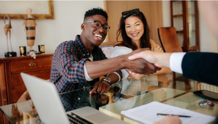 Happy property owners shaking hands with real estate broker after a deal. Young couple handshaking real estate agent after signing contract.