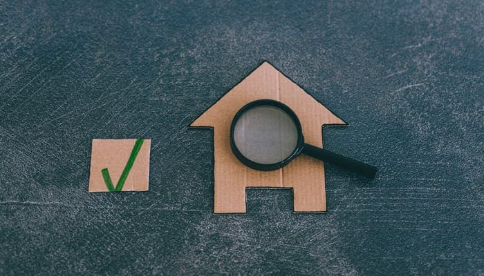 buying or moving house concept, miniature cardboard house with magnifying glass analyzing it as an image for a piece on we buy houses