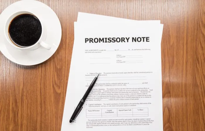 Promissory note sitting on a wooden desk with a cup of coffee to the left