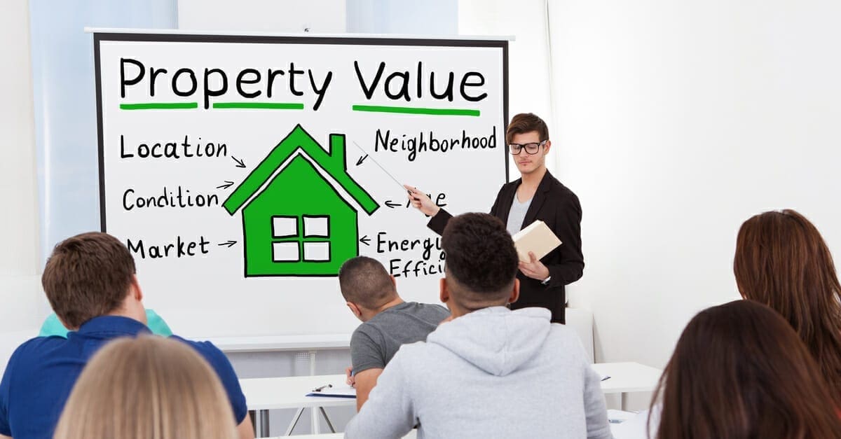 A teacher standing in the front of a classroom pointing at a whiteboard with a green house and some generic real estate terms as a featured image for a post on how long does it take to become a real estate agent