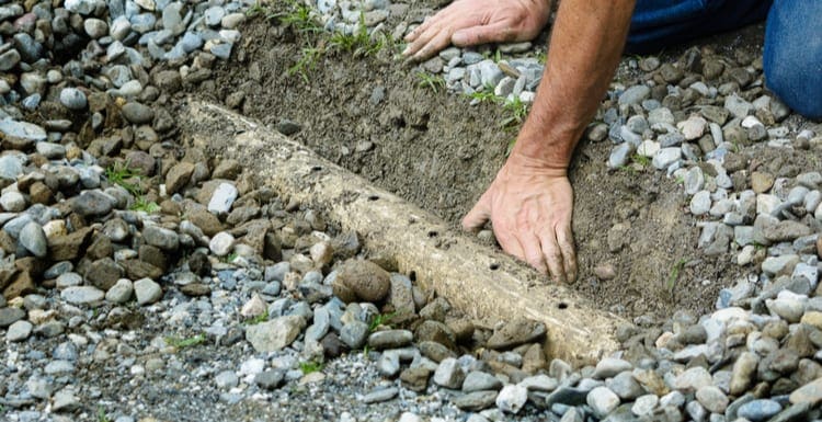 Man clears mud from drainage ditch in driveway as the featured image for a piece on what is a french drain