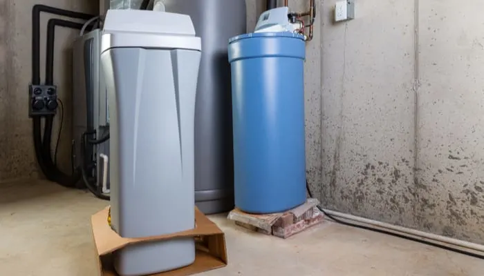 Old and new water softener tanks in a utility room waiting for replacement to remove minerals from hard water