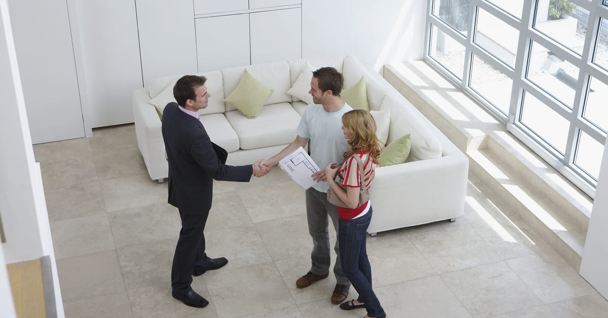 As an image for a piece on arms length transactions, image of an elevated view of a male real estate agent shaking hands with a man by woman in new home