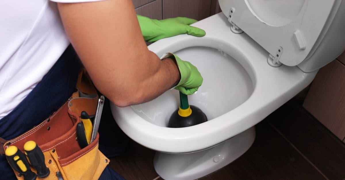 Plumber repairing toilet with hand plunger, closeup 