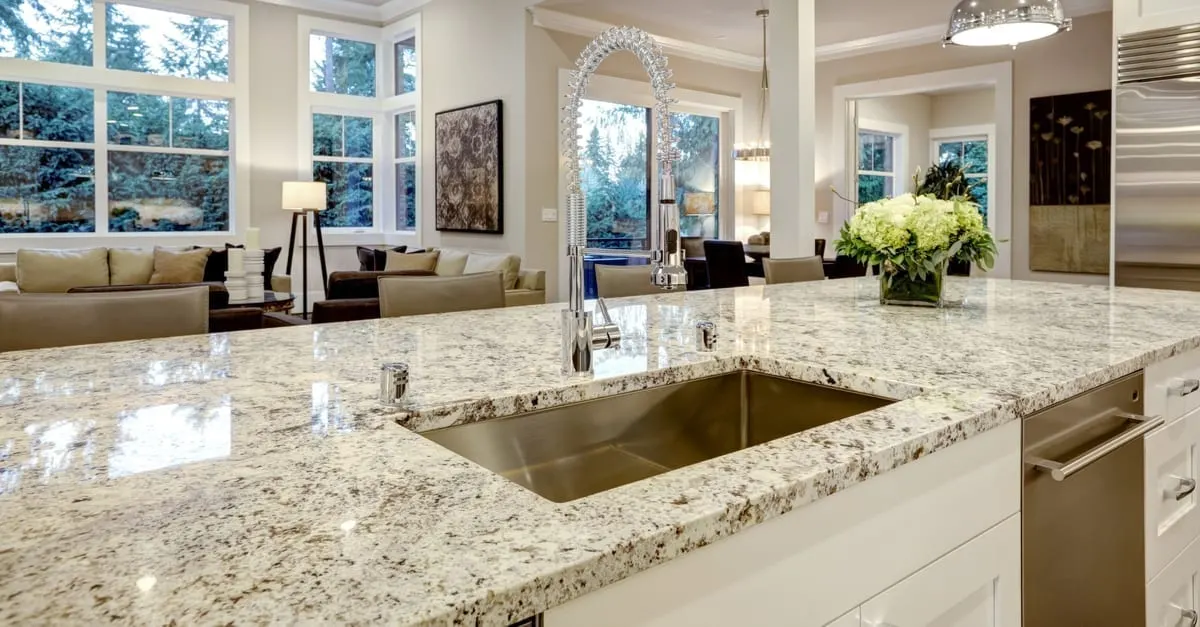 White kitchen design features large bar style kitchen island with granite countertop illuminated by modern pendant lights