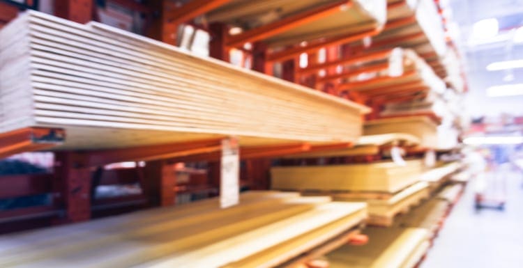 As a featured image for a piece on plywood sheet sizes, Blurred wooden bars from floor to ceiling at lumber yard of hardware store in America. Rack of pre-cut panel, mill wood timber, red oak, poplar, cedar, whitewood board, siding, plywood on flatbed cart