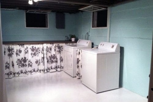 An unfinished basement with curtains, a washer/dryer combo, and a painted floor