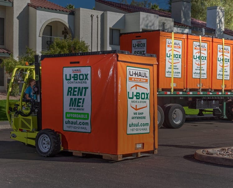 Picture of a Uhaul box sitting on a truck along with a forklift lifting one