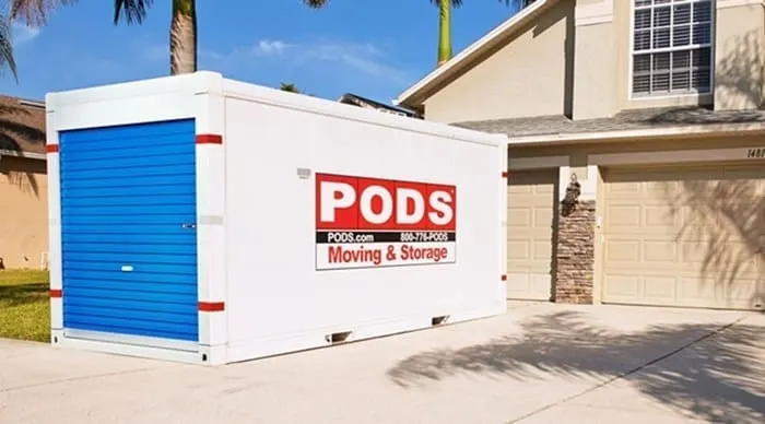 A PODS container sitting in the driveway of a tan house