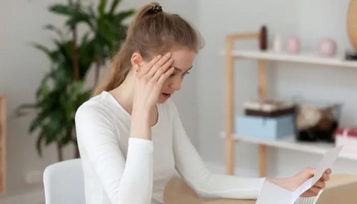 Frustrated millennial woman sitting at the desk in office or at home read notification about debt or not recruited. Stressed student holding letter about scholarship refusal expulsion from high school