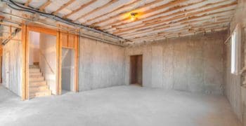 Featured image for a piece on unfinished basement ideas showing a drab cement walled basement with wooden framing by the stairs