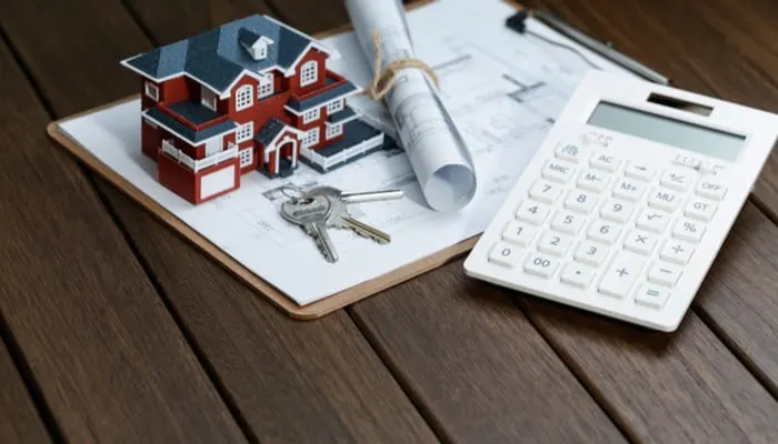 a calculator in front of a Villa house model with a blueprint as an image for a piece on Seller Carryback