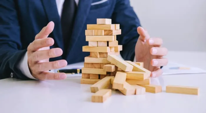 Wooden blocks falling down because a tax deed investment went awry and a man in a suit is putting his hands up in despair
