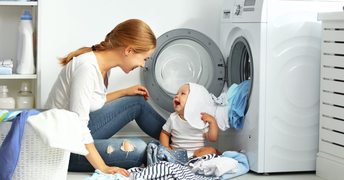 mother a housewife with a baby engaged in laundry fold clothes into the washing machine as the featured image for a piece on portable washing machines