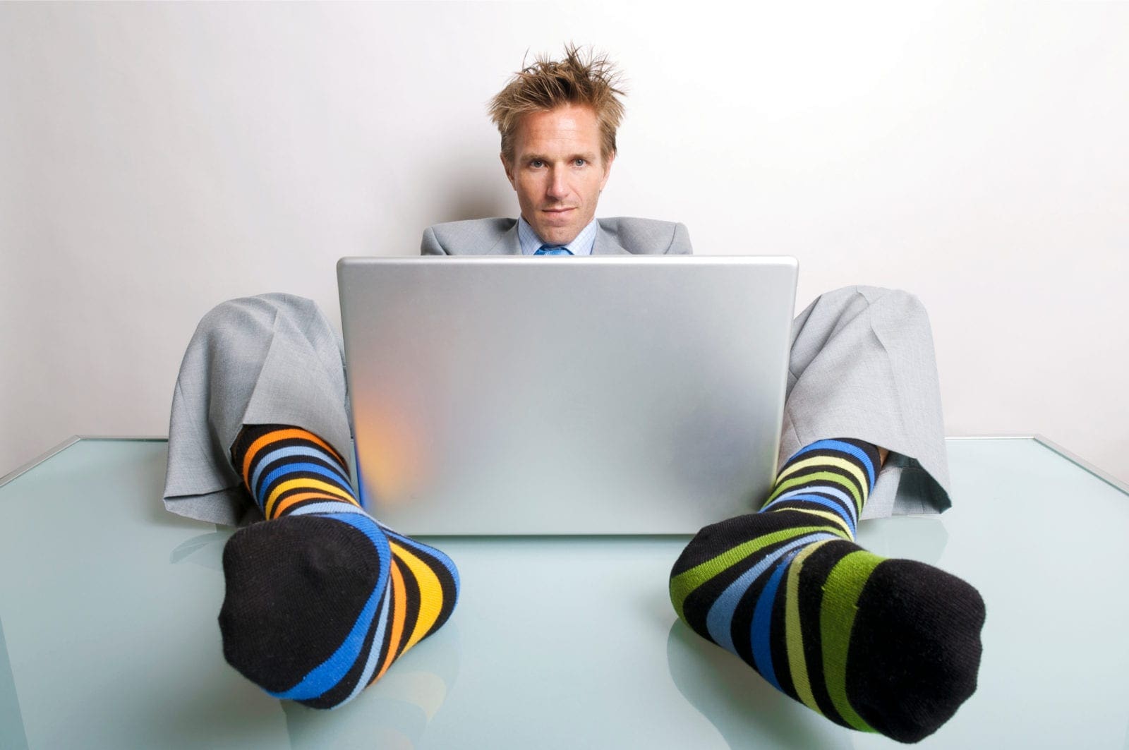 Unprofessional office worker slouching at his desk with his striped socks feet curled around his laptop as he types