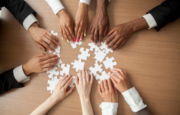 Hands of diverse people connecting puzzle together on office desk, multi-ethnic team engaging in finding best business solutions for successful teamwork, teambuilding unity concept, top close up view