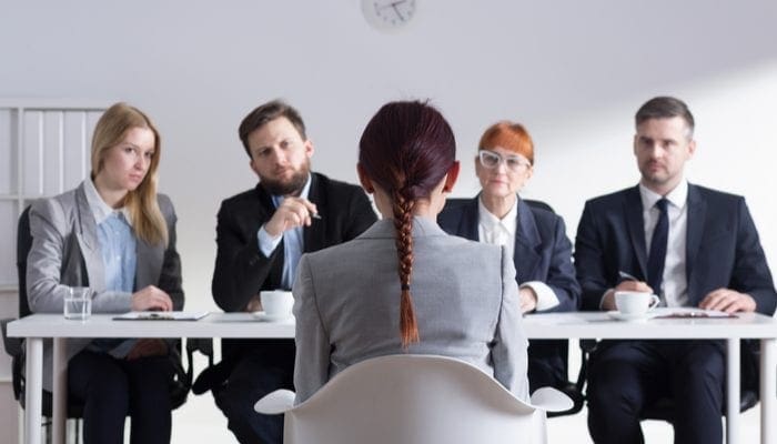 Woman during job interview and four elegant members of management to symbolize the opportunity and pros and cons of becoming a real estate agent