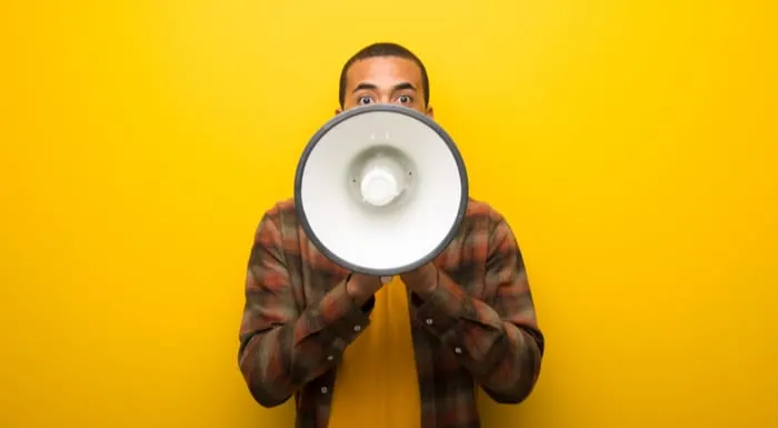Young african american man on vibrant yellow background shouting through a megaphone to announce a new real estate agent bio