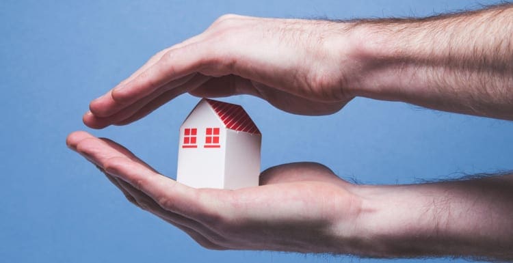 Hands covering a toy house. Home protection concept as the featured image for a piece on what does a home warranty cover