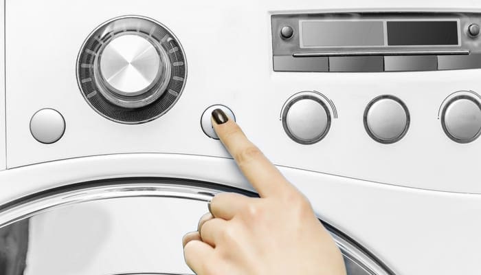 A woman's hand presses a button on the washing machine. Start the wash cycle.
