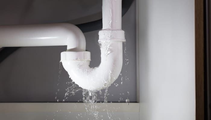 Close-up Of Water Is Leaking From The White Sink Pipe to symbolize finding a water leak from the bottom of a garbage disposal