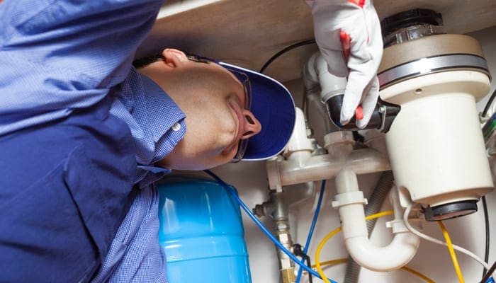 Portrait of a plumber at work on a garbage disposal leaking from bottom