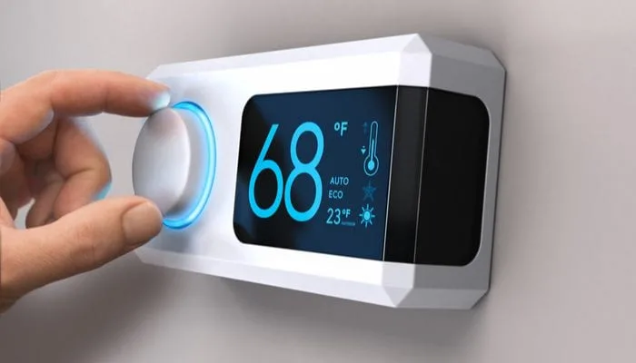 Hand turning a home thermostat knob to set temperature on energy saving mode. fahrenheit units. Composite image between a photography and a 3D background.
