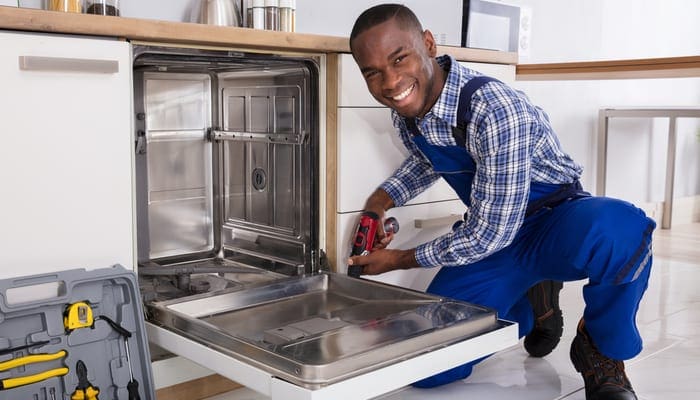 Young African Repairman Fixing Dishwasher In Kitchen as an image for a piece on standing water in dishwasher