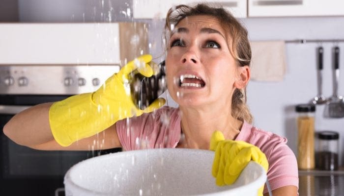 As an image for a piece on "plumbers near me," Shocked Woman Calling Plumber While Collecting Water Leaking From Ceiling Using Utensil