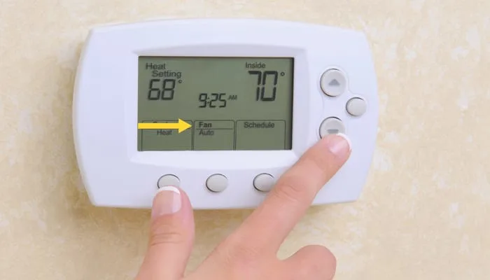 Closeup of a woman's hand setting the room temperature on a modern programmable thermostat.