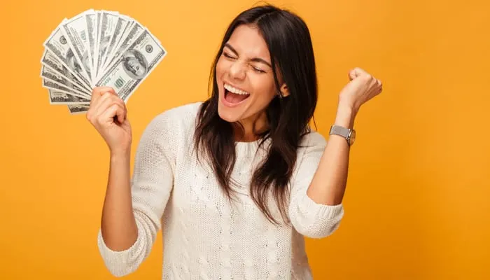 Portrait of a cheerful young woman holding money banknotes and celebrating isolated over yellow background as a part-time real estate agent earnings