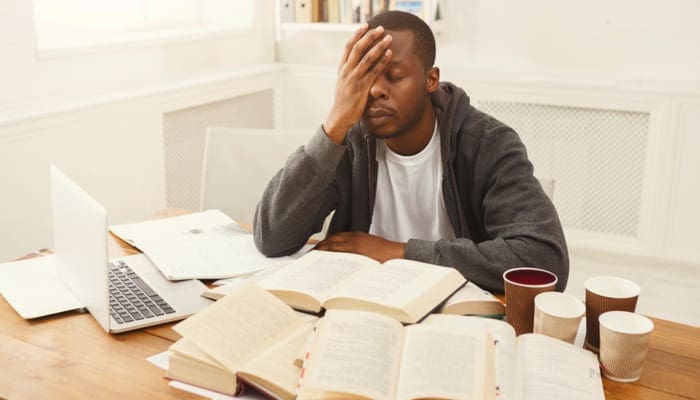 A student taking a real estate crash course near me sitting at a desk with various study materials holds his hand up to his face
