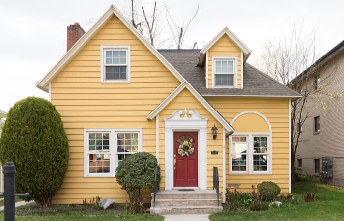 Yellow single family home with red door and floral wreath as an image for a piece on patio homes