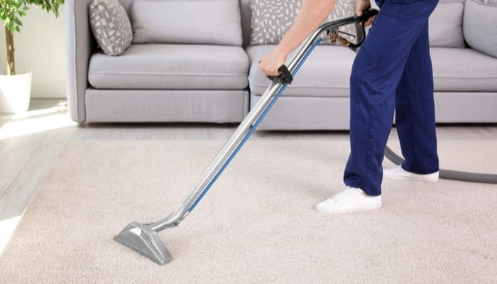 Male worker removing dirt from carpet with professional vacuum cleaner indoors