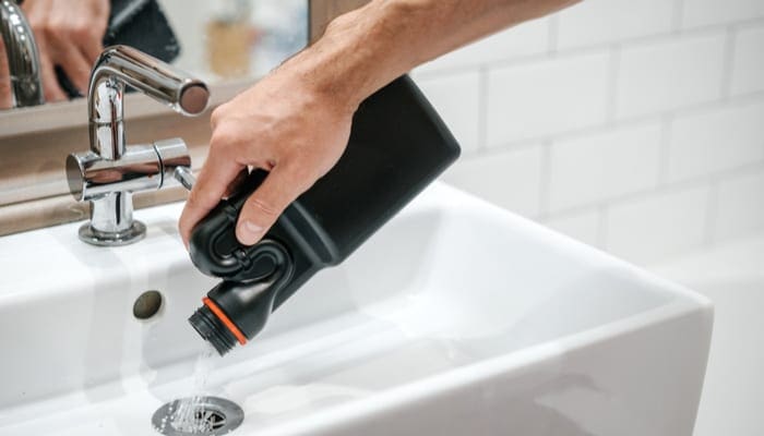 Removal of blockage in the sink, the hand of a man with a bottle of a special remedy with granules. Clean the blockages in the bathroom with chemicals.