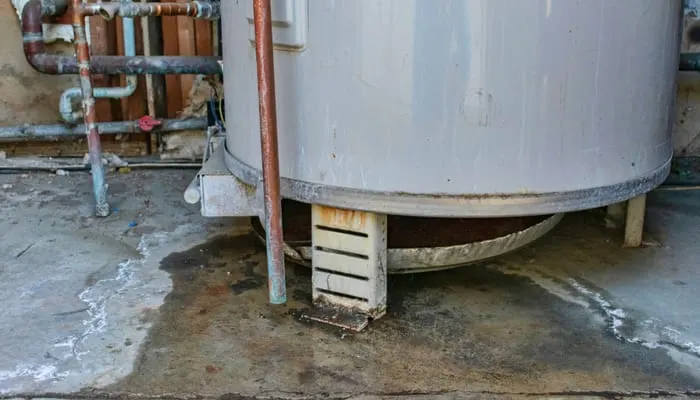 Water heater leaks from the bottom to the floor. Overflowing water heater drip pan. It is time to call a plumber service for inspection, repair or replacement