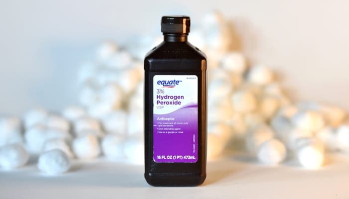 A bottle of Equate brand hydrogen peroxide with a pile of cotton balls in the background