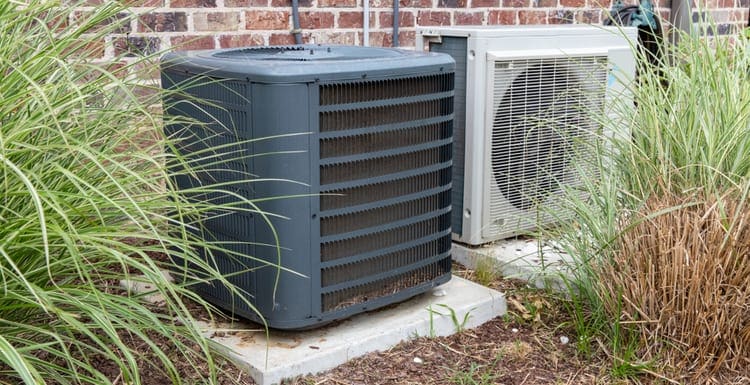 HVAC Air Conditioner Compressor and a Mini-split system together next to each other, next to a brick home as a featured image for a piece on ac leaking water