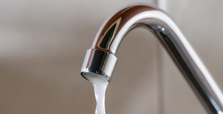 Horizontal image of a tap with water flowing slowly during a period of scarcity due to low water pressure