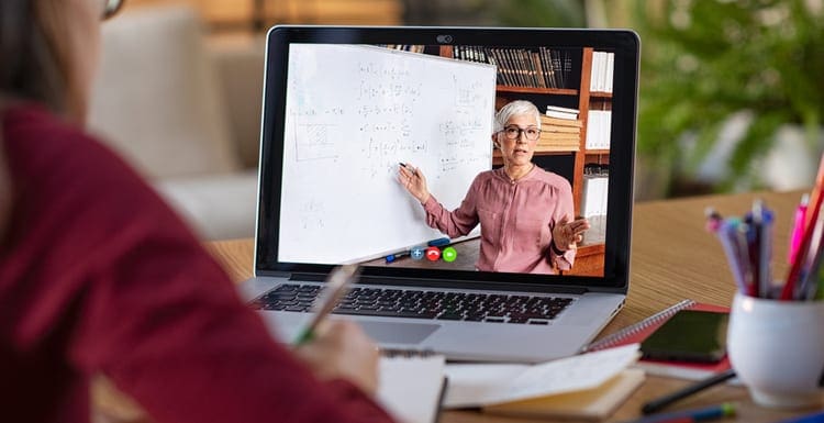 As an image for a piece on real estate crash course near me, Young student watching lesson online and studying from home. Young woman taking notes while looking at computer screen following professor doing math on video call. Girl studying from home on pc.