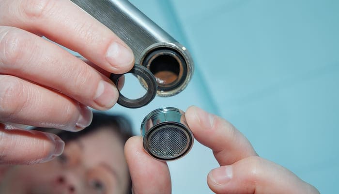Woman plumber repairing a clogged kitchen sink aerator to fix a low water pressure issue