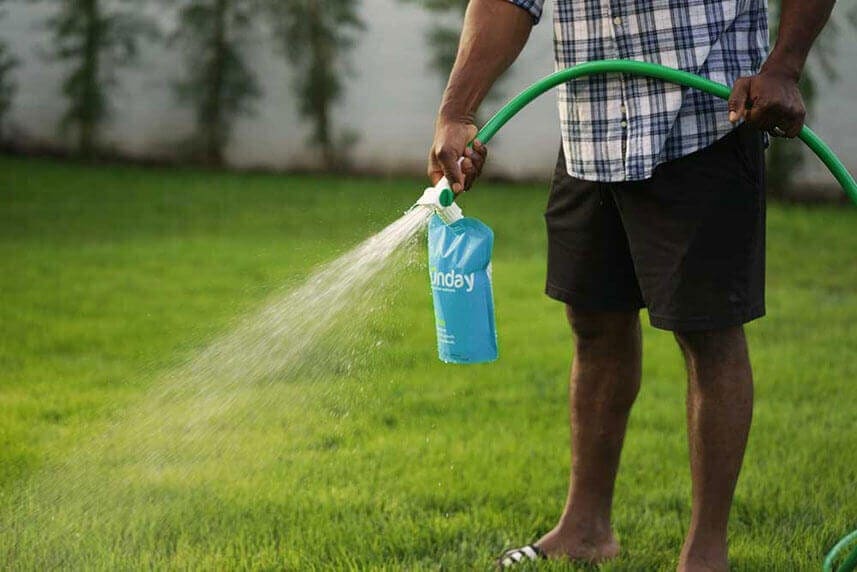 Man with hose spraying a Sunday lawn care product on his grass