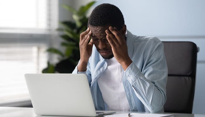 Stressed office worker sit at desk near computer touching temples closed eyes feels unhealthy suffers from headache, solving business problem, tired employee working on difficult task concept