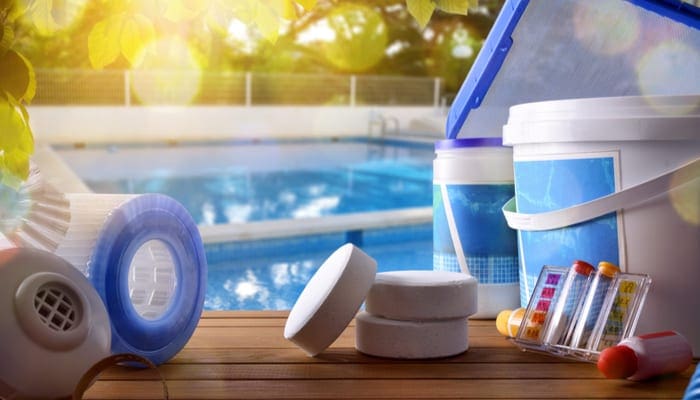 To prevent a green pool, Swimming pool service and equipment with chemical cleaning products and tools on wood table and pool background. Horizontal composition. Front view