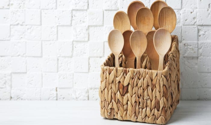 Wooden spoons in wicker basket on table against white wall