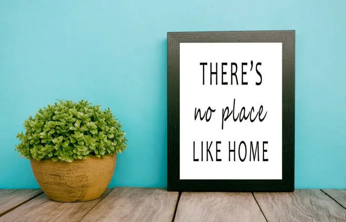 a sign sits on a desk alongside a plant with a quote about home on the framed paper